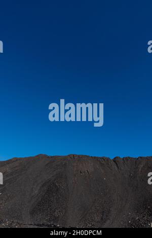 Ein Haufen von Mineralstoffen in Kohlekraftwerken. Das an einem sonnigen Tag aufgenommene Foto kontrastiert das Schwarz der Kohle mit dem Blau des Himmels. Stockfoto