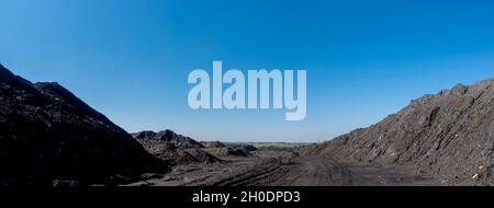 Ein Haufen von Mineralstoffen in Kohlekraftwerken. Das an einem sonnigen Tag aufgenommene Foto kontrastiert das Schwarz der Kohle mit dem Blau des Himmels. Stockfoto