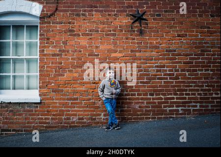 Kleiner Junge mit großem Lutscher, der sich an einer alten Backsteinmauer lehnt Stockfoto