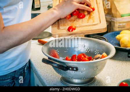 Eine Frau gießt geschnittene Tomaten in einen Sieb, während sie das Abendessen kocht Stockfoto