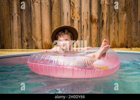 Kleiner Junge in Cowboyhut, der sich in einem Hinterhof-Pool abkühlt. Stockfoto