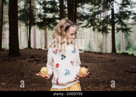 Mädchen jongliert im Herbst im Wald mit Äpfeln Stockfoto