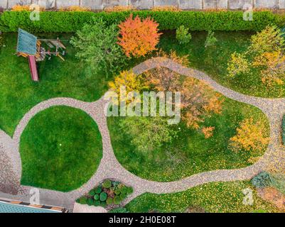 Luftaufnahme des Spazierwegs zwischen bunten hellen lebendigen Gartenbaum zuerst gefallenen trockenen Blättern auf grünem Gras Rasen auf dem Haushof oder Stadtpark in Stockfoto