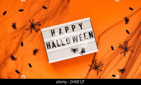 Whiteboard für Text mit dem Wort Happy Halloween, Fledermäuse und Spinnen im Spinnennetz auf orangefarbenem Hintergrund, Draufsicht, flach liegend. Konzeptkarte für den Stockfoto