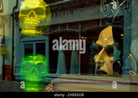 Eine gruselige Szene materialisiert sich in der Reflexion eines Schaufensters mit Schädeln und einem gruseligen Gesicht. Konzept des Todes der Hauptstraße vielleicht. Stockfoto