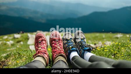 Junges Paar, das in den Bergen zeltet. Touristen Füße in Trekkingstiefeln entspannen sich nach einer langen Wanderung auf der Spitze des Hügels an sonnigen Tagen. Urlaub und Reisen Stockfoto