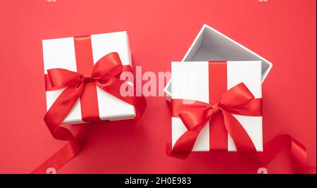 Weihnachtsgeschenke Überraschung, zwei Valentine Geschenk-Boxen weiß mit rotem Band Schleife geöffnet und geschlossen auf rotem Hintergrund, Neujahr Urlaub Verpackung Pac Stockfoto