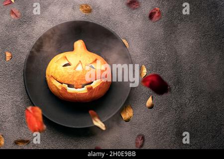 Ein gruseliger orangefarbener Kürbis auf dem Tisch, leuchtende Augen, ein schwarzer Teller und ein Hintergrund. halloween Party Einladung in ein Restaurant oder zu einer Feier in einem Stockfoto