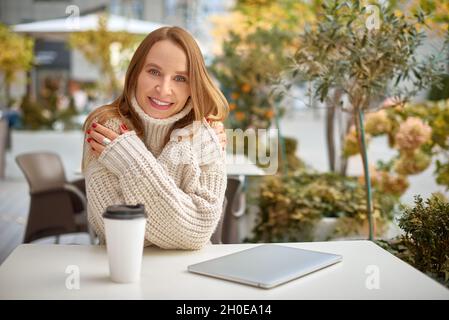Frau in Grobstrick Pullover trinken Kaffee und wärmt sich in der Stadt Café. Warme Farben horizontalen Foto Stockfoto