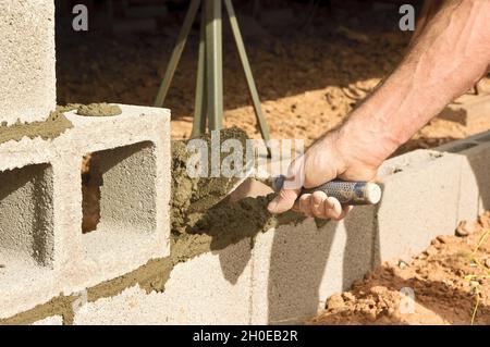 Die Hand eines Bauarbeiters bewegt eine Kelle, um frischen Mörtel auf einige Zementblöcke zu legen. Stockfoto