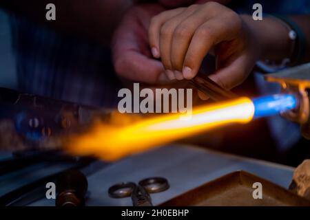 Eine Hand eines Flammenarbeiters und eine Hand eines Kindes während der Herstellung von Glasperlen.Diese Kunst wurde 2020 in die repräsentative Liste des Immateriellen aufgenommen Stockfoto