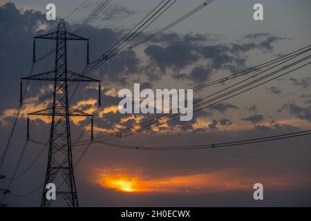 Masten und Stromleitungen bei Sonnenuntergang auf den Sümpfen von Higham Kent. Stockfoto