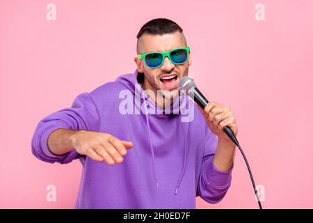 Foto von coolen jungen Brunet Kerl singen in Mic Wear Brillen Hoodie isoliert auf rosa Hintergrund Stockfoto