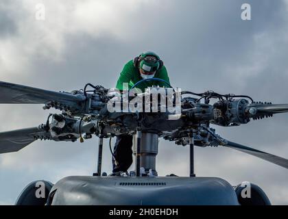 SÜDCHINESISCHES MEER (FEB 12, 2021) U.S. Navy Aviation Structural Mechanic 2nd Class James Han, aus Tian Jin, China, zugewiesen an die „Magier“ des Hubschrauber-Seeschlagergeschwaders (HSM) 35, Ersetzt eine Hydraulikleitung auf dem oberen Rotor eines MH-60R Sea Hawk auf dem Flugdeck des Arleigh Burke-Klasse Lenkflugkörper-Zerstörers USS John Finn (DDG 113) 12. Februar 2021. John Finn, Teil der Theodore Roosevelt Carrier Strike Group, ist im geplanten Einsatzgebiet der 7. US-Flotte unterwegs. Da die US Navy die größte vorwärtseingesetzte Flotte ist, arbeitet die 7th Fleet routinemäßig und interagiert mit ihr Stockfoto