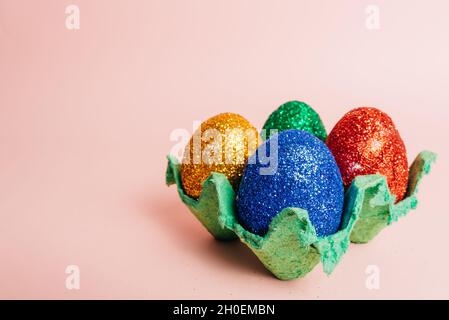 Eier bedeckt mit buntem Glitzer in grünem Nest vor rosa Hintergrund Stockfoto