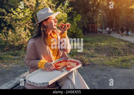Modische junge Frau mit Pizza im Herbst Park. Genießen Sie ein Stück Pepperoni im Freien. Essen heiße Snacks Stockfoto