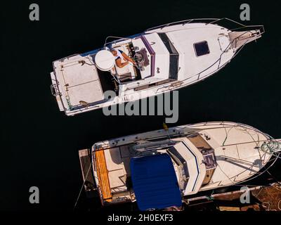 In der Nähe des Piers stehen zwei Boote. Ein junges Mädchen sitzt auf einem Boot. Drohnenfoto von oben. Stockfoto