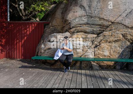 Eine Asiatin mittleren Alters telefoniert vor einem massiven Felsen Stockfoto