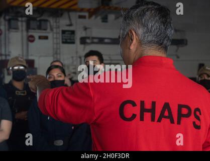 210220-N-DQ752-1009 PAZIFISCHER OZEAN (FEB 20, 2021) Bef. Samuel Contreras gibt die Eröffnungsrede für eine Taufe in der Hangarbucht des Flugzeugträgers USS Nimitz (CVN 68). Nimitz, das Flaggschiff der Nimitz Carrier Strike Group, führt derzeit Routineoperationen in der dritten US-Flotte durch. Stockfoto