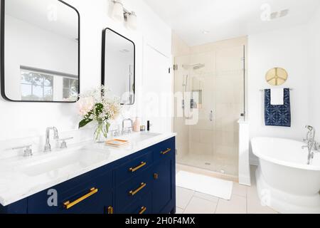 Das wunderschön renovierte Badezimmer verfügt über einen blauen Schminkschrank, eine geflieste Dusche und eine separate Badewanne. Stockfoto