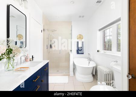 Das wunderschön renovierte Badezimmer verfügt über einen blauen Schminkschrank, eine geflieste Dusche und eine separate Badewanne. Stockfoto