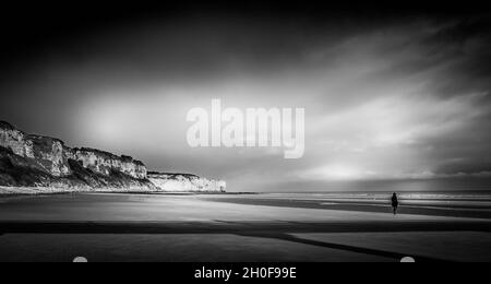 Schwarz-Weiß-Bild von Einzelfigur am Strand von Utah Normandie Frankreich. Mit Klippen, Strand, Meer und herrlichem Himmel. Stockfoto