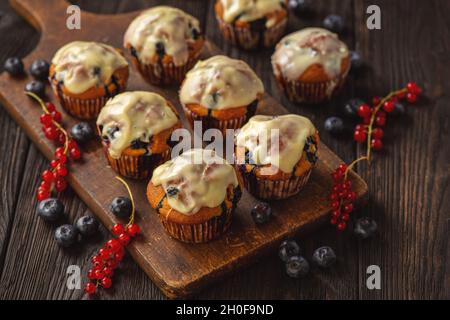 Hausgemachte Muffins mit roten Johannisbeeren und Blaubeeren, bedeckt mit weißer Schokolade. Stockfoto