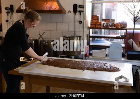 Eine Frau, die Fudge, eine Art Süßwaren, im Inneren von Rolys Fudge Pantry-Laden, Looe, Cornwall, Großbritannien, macht Stockfoto