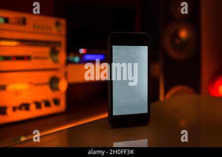 Smartphone als Fernbedienung für Home Sound System. Farbenfroher Hintergrund mit Lautsprechern und Verstärker Stockfoto