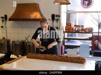 Eine Frau, die Fudge, eine Art Süßwaren, im Inneren von Rolys Fudge Pantry-Laden, Looe, Cornwall, Großbritannien, macht Stockfoto