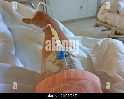 Peripherer Venenkatheter in der Vena der menschlichen Hand. Medizinische Therapie und Hilfe für die Person, die im Bett des Krankenhauszimmers liegt. Stockfoto