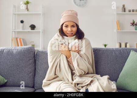 Frau in einem hellen Wohnzimmer in der Wohnung in ein kariertes Karo gehüllt, das unter der Kälte leidet. Stockfoto