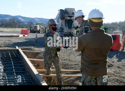 Das Marinebataillon 5 mit Sitz in Port Hueneme, Kalifornien, baute im Februar 2021 zwei Wochen lang im Trainingsgebiet 10 von Fort Hunter Liggett eine Betonunterlage. FHL Commander Col. Charles Bell überreichte vier vom NMCB 6-Offizier identifizierten Seabees eine Challenge-Münze für ihren außergewöhnlichen Dienst. Baumeister Kleinoffizier 3. Klasse Gerou erhält Münze von Bell. Stockfoto