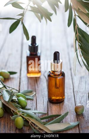 Olivfarbene kosmetische Bernsteinflaschen mit Serum oder Lotion auf Holzhintergrund mit Zweigen aus Olivenbaum. Stockfoto