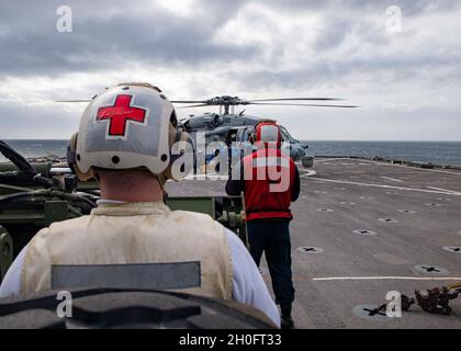 210226-N-NQ285-1210 ATLANTIK (FEB 26, 2021) Hospital Corpsman 1. Klasse Eric Lewis, links, aus Pensacola, Florida und dem Harpers Ferry-Klasse-Dock-Landungsschiff USS Carter Hall (LSD 50) zugewiesen, bietet medizinische Versorgung während eines Personentransfers in einem Hubschrauber der MH-60S Sea Hawk, der den „Chargers“ des Helicopter Sea Combat Squadron (HSC) 26 zugewiesen wurde, Auf dem Flugdeck des Schiffes, 26. Februar 2021. Carter Hall führt als Teil der Iwo Jima Amphibious Ready Group ein Training mit dem Amphibiengeschwader 4 und der 24. Marine Expeditionary Unit (24. MEU) durch. Stockfoto