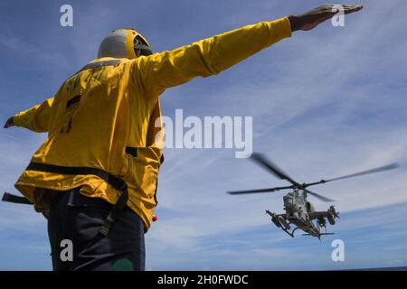 210227-N-UM706-1111 PHILIPPINISCHES MEER (FEB 27, 2021) der Mate 2nd Class Jeremiah Nortey von Boatswain aus Bronx, N.Y., signalisiert einen Bell AH-1W Super Cobra Hubschrauber, der dem Marine Medium Tiltrotor Squadron (VMM) 262 an Bord des Amphibiendocks USS Ashland (LSD 48) zugewiesen wurde. Ashland, Teil der America Amphibious Ready Group, arbeitet zusammen mit der 31. Marine Expeditionary Unit im Verantwortungsbereich der 7. US-Flotte, um die Interoperabilität mit Verbündeten und Partnern zu verbessern und dient als einsatzbereite Einsatztruppe zur Verteidigung von Frieden und Stabilität in der Indo-Pazifik-Region. Stockfoto