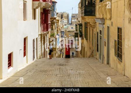 Typische Valletta Straßenarchitektur mit traditionellen maltesischen Holz eingezäunten Balkonen, schräg nach unten Straße und einem roten Briefkasten. Stockfoto