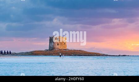 Atemberaubender Sonnenaufgang über dem Aragonischen Turm mit ein paar Touristen, die die Landschaft vom Strand La Pelosa, Sardinien, Italien aus genießen. Stockfoto