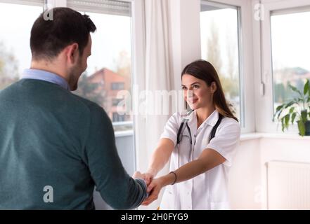 Junge Ärztin schüttelt sich die Hände mit einem männlichen Patienten im Büro Stockfoto
