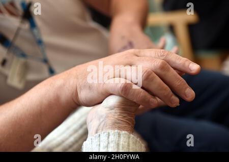 Nahaufnahme der Hände von Bewohnern in einem Pfleheim mit einem Mitarbeiter in Großbritannien Stockfoto