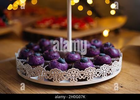 Schokoladen-Cupcakes mit violetter Creme und Heidelbeeren darauf. Im Hintergrund ein Bokeh-Effekt der gelben Lichter. Stockfoto