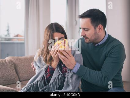 Freund kümmert sich um Mädchen mit Grippe. Sitzen auf dem Sofa zu Hause mit Decke bedeckt und Tee trinken Stockfoto