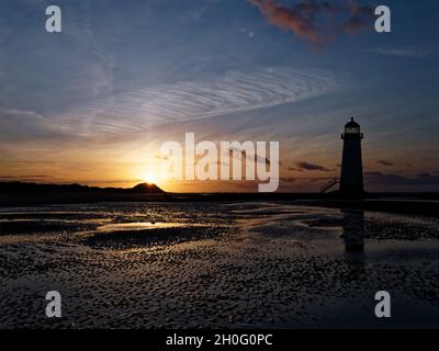 Die Sonne geht hinter den Dünen gegen den Punkt des Ayr Lighthouse auf Talacre, Nordwales, unter. Stockfoto