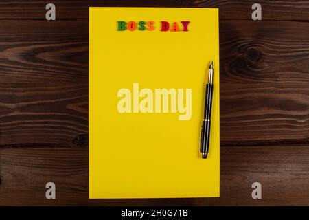 National Happy Boss Day. Bunte Buchstaben in einer gelben leeren Seite mit Stift auf dem Tisch. Grußkarte des Chefs mit Platz für die Kopie f Stockfoto