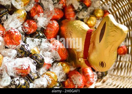 Der legendäre Lindt Chocolate Bunny, in Goldfolie mit markantem roten Kragen und Glocke gewickelt, in einem Weidenkorb mit Eiern und Lindor-Schokolade Stockfoto