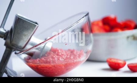 Altes Metall vintage manuelle Fleischwolf, Teller mit gehackten Tomaten, Topf mit Tomaten auf einem weißen Tisch. Hausgemachte Adjika, Home Preservation, ferm Stockfoto