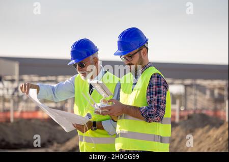 Zwei Ingenieure mit Helmen und Westen, die per Fernbedienung mit der Drohne arbeiten. Technologische Innovationen in der Bauindustrie Stockfoto