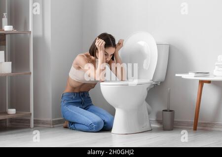 Junge Frau in der Nähe von Toilettenschüssel im Badezimmer. Anorexie-Konzept Stockfoto