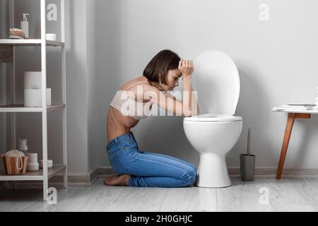 Junge Frau in der Nähe von Toilettenschüssel im Badezimmer. Anorexie-Konzept Stockfoto