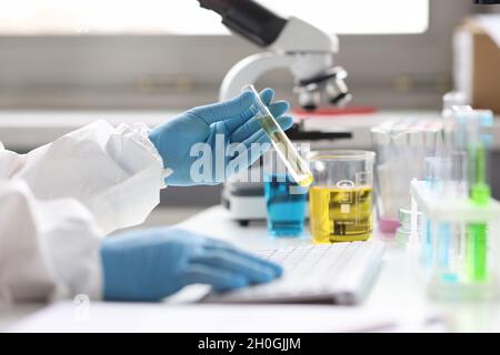 Der Wissenschaftler hält das Reagenzglas mit durchsichtiger Flüssigkeit und Typen auf der Tastatur Stockfoto